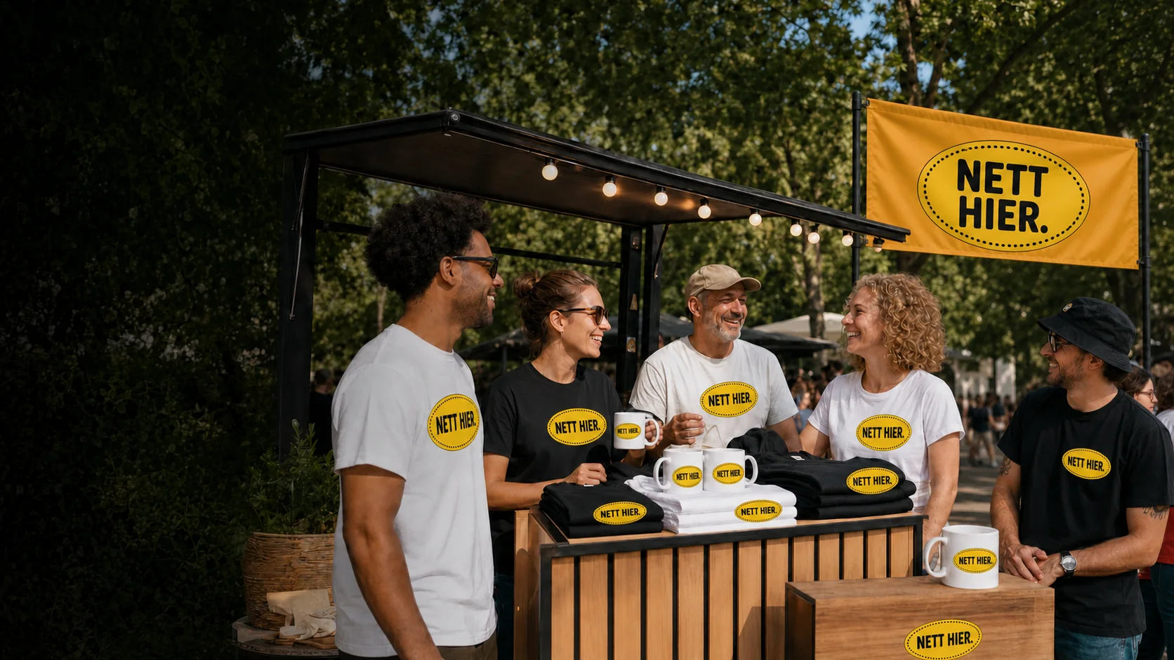Team an einem sommerlichen Eventstand mit Nett hier Aufklebern, Tassen, Shirts und Fahne